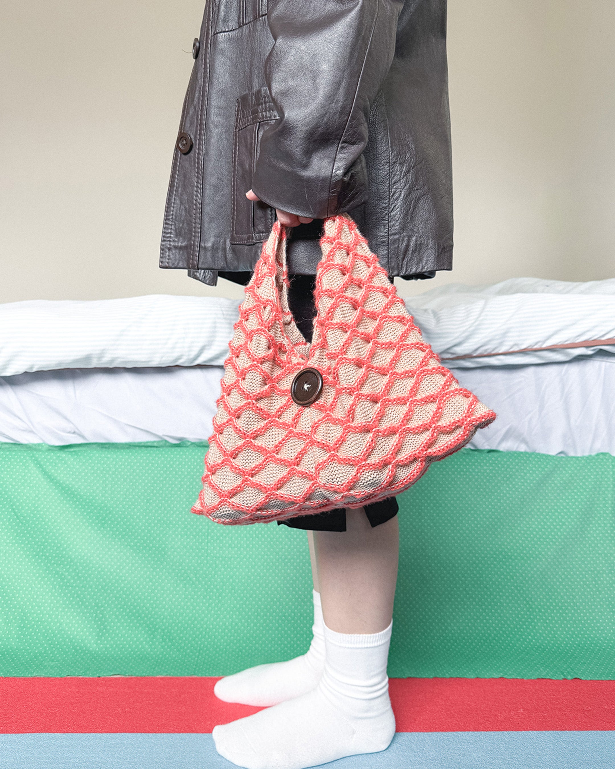Person holding a handmade knitted bag with textured pattern, styled in a casual outfit indoors