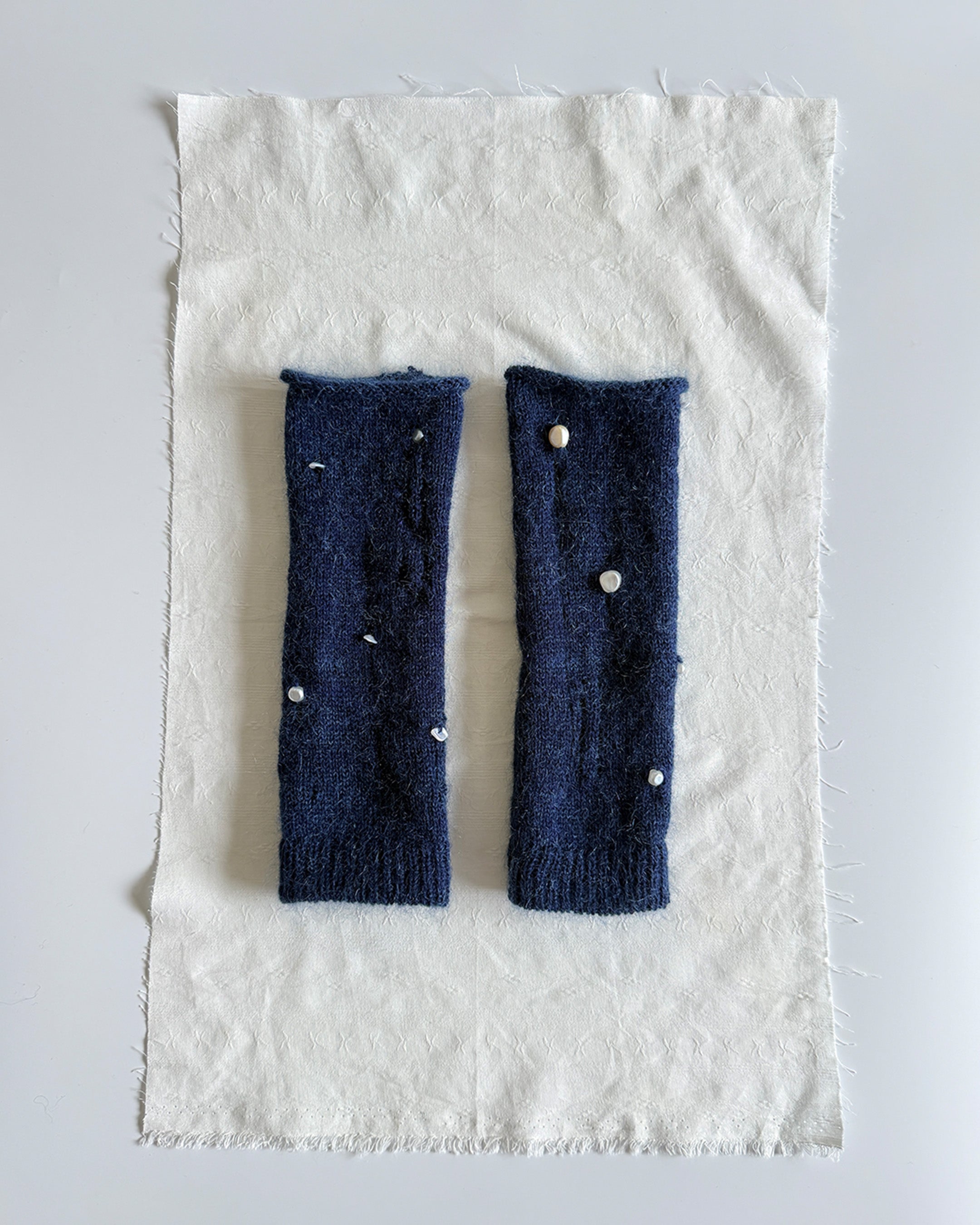 navy knit gloves with pearl details, merino wool and mohair texture close-up of handmade pearl gloves on neutral background soft knit fingerless gloves with pearl accents, wool mohair blend