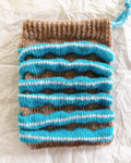 knit pouch with soft textured stripes in blue and brown
flat lay of wool knit pouch on crinkled fabric background
small handmade knit bag with mohair texture detail