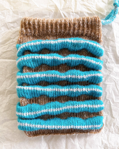 knit pouch with soft textured stripes in blue and brown
flat lay of wool knit pouch on crinkled fabric background
small handmade knit bag with mohair texture detail